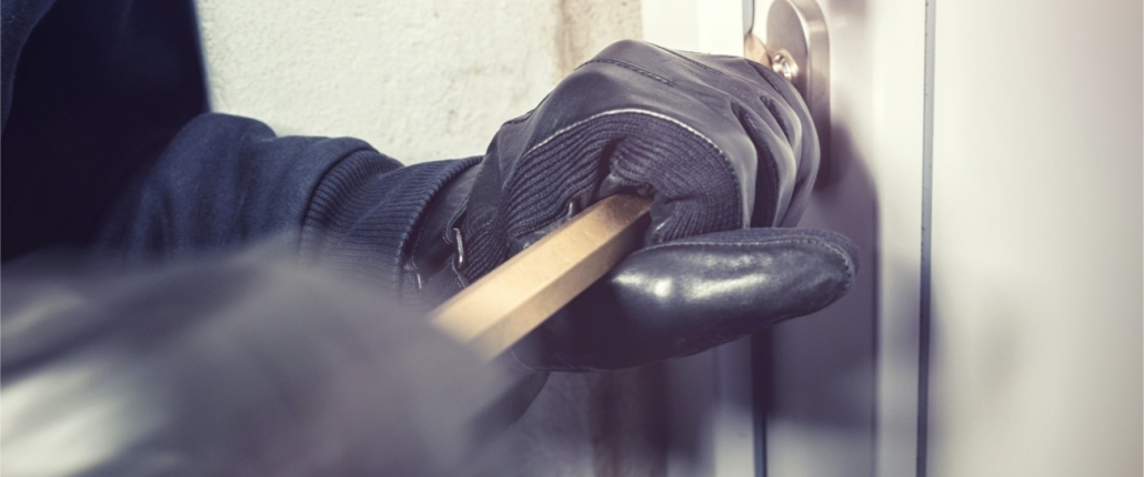Gloved hands holding a crowbar, breaking open a door.