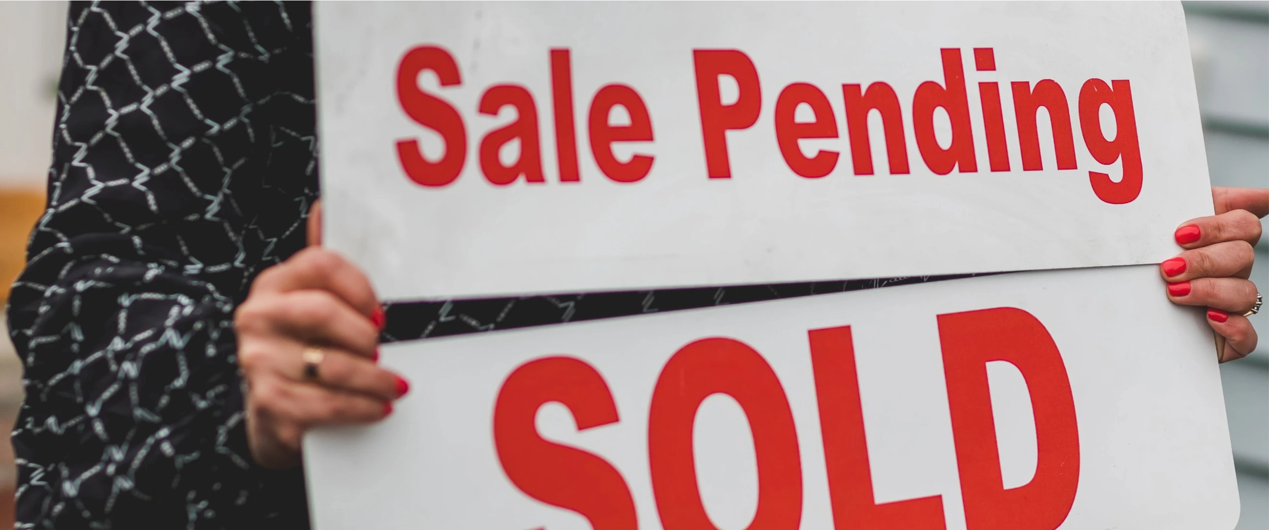 A dramatic close up of a woman holding "Sale pending, SOLD" signs